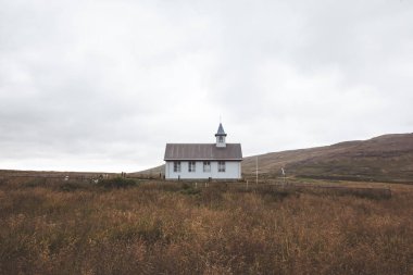Tuhaf beyaz kilise bulutlu bir gökyüzünün altındaki bir tarlada huzur içinde oturuyor. Yuvarlanan tepelerle çevrili sahne, İzlanda kırsalında basitlik ve kırsal cazibe yayıyor. Snaefellsnes Yarımadası.