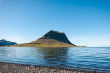 Kirkjufell, Batı İzlanda 'daki Snafellsnes Yarımadası' ndaki ikonik dağ, sakin sularda yansımasıyla görkemli bir şekilde duruyor, yumuşak, pastel bir gökyüzünün altında..