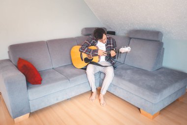 Çıplak ayaklı müzisyen gri bir koltukta rahat bir şekilde oturur, rahat bir atmosferde akustik gitar tıngırdatır, rahatlatıcı melodilerde kaybolur ve müziğe derin duygusal bağlar kurar..