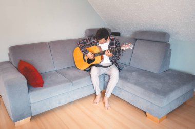 Çıplak ayaklı müzisyen gri bir koltukta rahat bir şekilde oturur, rahat bir atmosferde akustik gitar tıngırdatır, rahatlatıcı melodilerde kaybolur ve müziğe derin duygusal bağlar kurar..