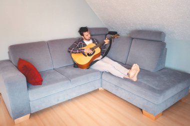 Çıplak ayaklı müzisyen gri bir koltukta rahat bir şekilde oturur, rahat bir atmosferde akustik gitar tıngırdatır, rahatlatıcı melodilerde kaybolur ve müziğe derin duygusal bağlar kurar..
