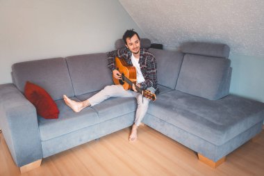 Çıplak ayaklı müzisyen gri bir koltukta rahat bir şekilde oturur, rahat bir atmosferde akustik gitar tıngırdatır, rahatlatıcı melodilerde kaybolur ve müziğe derin duygusal bağlar kurar..