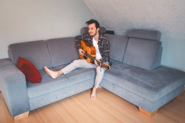 Çıplak ayaklı müzisyen gri bir koltukta rahat bir şekilde oturur, rahat bir atmosferde akustik gitar tıngırdatır, rahatlatıcı melodilerde kaybolur ve müziğe derin duygusal bağlar kurar..