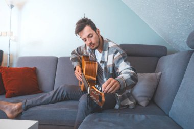 26 yaşındaki müzisyen, rahat bir mavi kanepede çıplak ayakla oturur, akustik bir gitar çalar, melodilerde kaybolur, yaratıcılıkla dolu rahat ve samimi bir atmosfer yaratır..