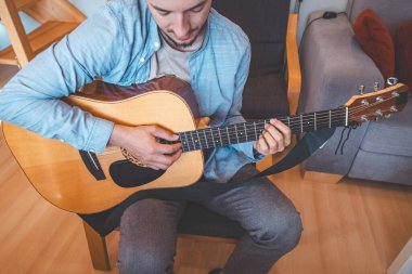 Müzisyen tıngırtılarına yakın çekim, rahat bir evde akustik gitar, müziğe dalmış. Onun günlük tarzı, sıcak aydınlatma ve rahat atmosferi huzurlu, sanatsal ve ilham verici bir an yaratıyor..