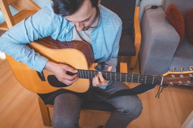 Müzisyen tıngırtılarına yakın çekim, rahat bir evde akustik gitar, müziğe dalmış. Onun günlük tarzı, sıcak aydınlatma ve rahat atmosferi huzurlu, sanatsal ve ilham verici bir an yaratıyor..