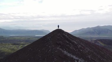 Explorer soyu tükenmiş bir volkanın zirvesinde duruyor. Batı İzlanda 'daki Snaefellsnes Yarımadası' ndaki bir vadiye bakıyor. İnanılmaz bir doğa. İyileşme. 4K yatay video