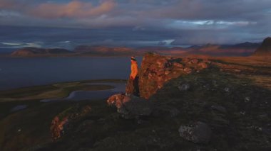 Dünyanın kıyısında, son uçurumun kıyısında İzlanda Snaefellsnes Yarımadası boyunca okyanusa dalıyor. İnsanlar korku içinde durup okyanusun derinliklerine bakarlar. Gökyüzü nefes kesen bir günbatımıyla yanarken..