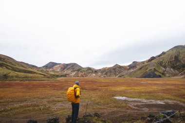 Gezgin, İzlanda Dağları 'nda yosunlu kayalar ve uzak ryolite zirveleriyle çevrili engebeli bir lav tarlasında yürüyor. İzlanda 'nın vahşi kalbinde gerçeküstü bir yolculuk.