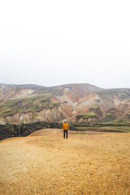 Yürüyüşçü, İzlanda Dağları 'ndaki Landmannalaugar' ın renkli ryolite dağları boyunca kum ve taş yol boyunca yürüyor. Vahşi volkanik güzelliğe barışçıl bir yolculuk..