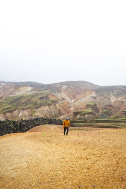 Yürüyüşçü, İzlanda Dağları 'ndaki Landmannalaugar' ın renkli ryolite dağları boyunca kum ve taş yol boyunca yürüyor. Vahşi volkanik güzelliğe barışçıl bir yolculuk..