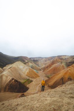 İzlanda, Landmannalaugar 'daki renkli bir rhyolite vadisinin kenarında duran yalnız yürüyüşçü volkanik güçlerin şekillendirdiği uçsuz bucaksız gerçeküstü manzaraya bakıyor. Sisli ve yağmurlu.