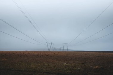 Elektrik hatları sisli İzlanda düzlükleri boyunca uzanıyor ve sisin içinde kayboluyor. Karamsar, minimalist bir manzara izolasyonu ve vahşi doğada insan varlığını yakalıyor..