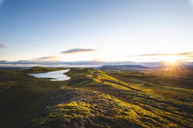 Hrunamannahreppur, İzlanda 'daki Hrunamannahreppur Dağı yakınlarındaki sakin göl ve yuvarlanan tepeler üzerinde altın saat. İzlanda kırsalında huzurlu bir günbatımı anı.