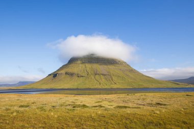 Snaefellsnes Yarımadası, İzlanda 'daki Iconic Kirkjufell Dağı, açık mavi gökyüzü altında alçak asılı bir bulut tacı ve canlı sonbahar tonları ile. Kilise dağı ünlü bir yerdir..