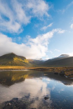 Snaefellsnes Yarımadası, İzlanda 'daki Grundarfjordur yakınlarındaki manzara dağları dramatik bulutlar ve göldeki yansımalarla altın ışıkta parlıyordu. İzlanda ve kuzey üzerinde gün batımı.