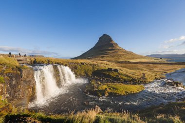 Kirkjufell Dağı, gün doğumunda altın çayırlar ve yumuşak bulutlarla Snaefellsnes Yarımadası 'nda barışçıl ve ikonik bir İzlanda manzarası yaratır..