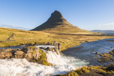 Kirkjufell Dağı, gün doğumunda altın çayırlar ve yumuşak bulutlarla Snaefellsnes Yarımadası 'nda barışçıl ve ikonik bir İzlanda manzarası yaratır..