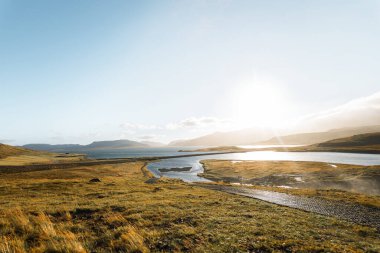 Kirkjufellfoss 'un arkasından Grundarfjordur' a doğru altın ışık saçıyor. Tepeleri, nehirleri ve kıyıları ılık tonlarda resmediyor. Yumuşak, ışıl ışıl İzlanda gökyüzünün altında..