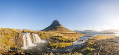 Kirkjufell Dağı, gün doğumunda altın çayırlar ve yumuşak bulutlarla Snaefellsnes Yarımadası 'nda barışçıl ve ikonik bir İzlanda manzarası yaratır..