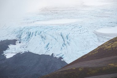 Karanlık volkanik yosunlu sırtlar ve yosunlu yamaçlar arasında İzlanda 'nın çarpıcı buzullarının yakın görüntüsü. Snaefellsnes Yarımadası 'nın göbeğinde buzdan ve topraktan oluşan çiğ bir zıtlık..