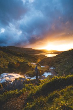 İnsan, İzlanda 'nın batısındaki Snaefellsnes Yarımadası' ndaki Selvallafoss şelalesinin soğuk ve berrak sularının altında duran büyülü günbatımının tadını çıkarıyor. Doğa hazinesi.