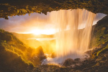 İzlanda 'nın batısındaki Snaefellsnes Yarımadası' nda Selvallafoss şelalesi. Arkasından yakalanan soğuk, berrak su çağlayanı gibi büyülü bir günbatımının önünde..