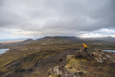 İzlanda 'nın Snaefellsnes yarımadasındaki Boynuz Dağı' nın sonunda tek başına yürüyen yürüyüşçü batan güneşten gelen altın ışık aşağıdaki engebeli volkanik araziyi aydınlatıyor. Kenarda dur..
