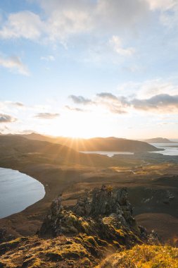 İzlanda 'nın Snaefellsnes yarımadasındaki Boynuz Dağı' nın sonunda tek başına yürüyen yürüyüşçü batan güneşten gelen altın ışık aşağıdaki engebeli volkanik araziyi aydınlatıyor. Kenarda dur..