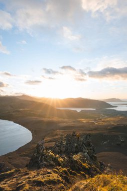 İzlanda 'nın Snaefellsnes yarımadasındaki Boynuz Dağı' nın sonunda tek başına yürüyen yürüyüşçü batan güneşten gelen altın ışık aşağıdaki engebeli volkanik araziyi aydınlatıyor. Kenarda dur..