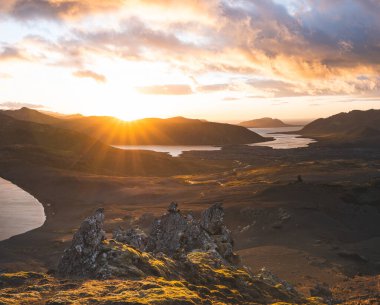 İzlanda 'nın Snaefellsnes yarımadasındaki Boynuz Dağı' nın sonunda tek başına yürüyen yürüyüşçü batan güneşten gelen altın ışık aşağıdaki engebeli volkanik araziyi aydınlatıyor. Kenarda dur..
