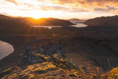 İzlanda 'nın Snaefellsnes yarımadasındaki Boynuz Dağı' nın sonunda tek başına yürüyen yürüyüşçü batan güneşten gelen altın ışık aşağıdaki engebeli volkanik araziyi aydınlatıyor. Kenarda dur..