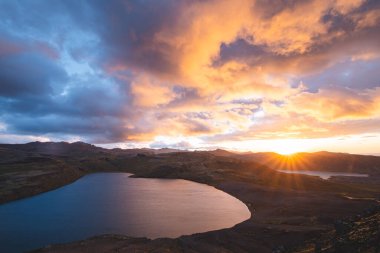 İzlanda 'daki Snaefellsnes yarımadasındaki bir dağ gölünün üzerinde altın güneş ışığı gökyüzüne ve aşağıdaki volkanik araziye çarpıcı bir ışık saçıyor. Masal günbatımı.