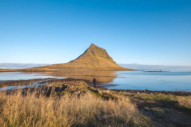 Yalnız gezgin, Snaefellsnes yarımadasındaki Kirkjufell 'e bakarak altın ışık ve yansımaların doğada huzurlu bir sabah anını şekillendirdiğini görür..