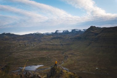 Sarı ceketli yürüyüşçü, İzlanda 'daki Kirkjufell Dağı' nın tepesinde doğan güneşi kucaklıyor. Fiyortların, vadilerin ve altın gökyüzünün üzerinde saf bir özgürlük anı yakalıyor..