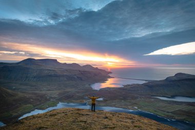 Sarı ceketli yürüyüşçü, İzlanda 'daki Kirkjufell Dağı' nın tepesinde doğan güneşi kucaklıyor. Fiyortların, vadilerin ve altın gökyüzünün üzerinde saf bir özgürlük anı yakalıyor..