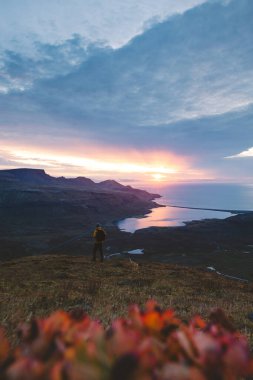 Sarı ceketli yürüyüşçü, İzlanda 'daki Kirkjufell Dağı' nın tepesinde doğan güneşi kucaklıyor. Fiyortların, vadilerin ve altın gökyüzünün üzerinde saf bir özgürlük anı yakalıyor..
