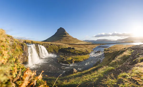 Kirkjufell Dağı, gün doğumunda altın çayırlar ve yumuşak bulutlarla Snaefellsnes Yarımadası 'nda barışçıl ve ikonik bir İzlanda manzarası yaratır..