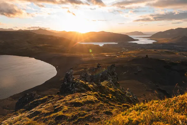 İzlanda 'nın Snaefellsnes yarımadasındaki Boynuz Dağı' nın sonunda tek başına yürüyen yürüyüşçü batan güneşten gelen altın ışık aşağıdaki engebeli volkanik araziyi aydınlatıyor. Kenarda dur..