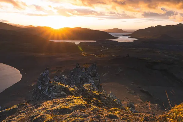 İzlanda 'nın Snaefellsnes yarımadasındaki Boynuz Dağı' nın sonunda tek başına yürüyen yürüyüşçü batan güneşten gelen altın ışık aşağıdaki engebeli volkanik araziyi aydınlatıyor. Kenarda dur..