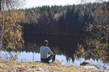İnsan Oslo Marka 'daki orman gölünün kıyısında dinlenir. Doğanın sessiz güzellikleriyle ıslanır ve Norveç' in vahşi doğasının sessizliğini yansıtır..