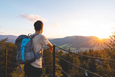 Sırt çantası altın saatinde bir platformda duruyor. Jeseniky Dağları 'nın ormanlık tepelerine ve vadilerine bakıyor. Sıcak günbatımı ışığında yıkanmış.