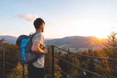 Sırt çantası altın saatinde bir platformda duruyor. Jeseniky Dağları 'nın ormanlık tepelerine ve vadilerine bakıyor. Sıcak günbatımı ışığında yıkanmış.