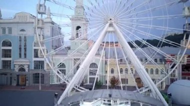Kiev. İnsansız hava aracı videosu. Büyük beyaz dönme dolap ve turistler Kiev 'in Podolsk bölgesindeki Kontraktova Meydanı' nın ortasında yürüyorlar.
