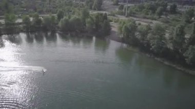 Cityscape with construction for weakboarding, Aerial shot of a cableway in a lake with a wakeboarder making turns and tricks. Sportsman grinding and rotating on a funbox. Girl wakeboarding in wake