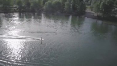 Cityscape with construction for weakboarding, Aerial shot of a cableway in a lake with a wakeboarder making turns and tricks. Sportsman grinding and rotating on a funbox. Girl wakeboarding in wake
