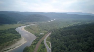 Aerial Drone View: Flight over pine tree forest and country road in sunset soft light. Mountain range in background. Nature, travel, holidays. Carpathians, Ukraine, Europe, Scenic aerial view 