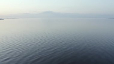 Geniş mavi göl arkaplanı ve aşağı bakan ılımlı dalgalar. Güneşli yaz gününde yeşil çayırlar arasında büyük mavi bir göl, Hava Aracı Uçuşu Güzel Gökyüzü ve Gün batımında Su