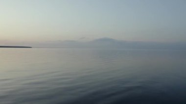 Geniş mavi göl arkaplanı ve aşağı bakan ılımlı dalgalar. Güneşli yaz gününde yeşil çayırlar arasında büyük mavi bir göl, Hava Aracı Uçuşu Güzel Gökyüzü ve Gün batımında Su