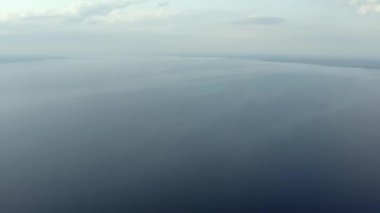 Small waves on calm water of big lake, bright yellow afterglow on clear sky. Aerial shot of Ladoga lake at summer evening, empty water surface until horizon line, neat colors of nature after sunset